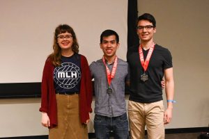 Katie O'Leary (a Major League Hacking Representative), Travis Chan, and Thomas Keady pose together at the front of Hodson 110. Chan and Keady have medals around their necks.