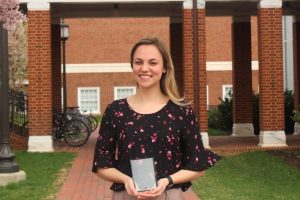 Kelly Culotta poses with a plaque outside of the breezeway between Hackerman and Malone Halls.