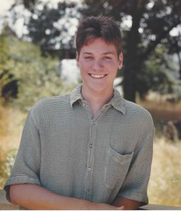 A young Cleve Pasarell stands in front of a field and trees.