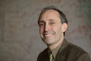 Headshot of Jason Eisner standing in front of a whiteboard.