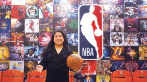 Paige Senal poses with a basketball in front of the NBA logo.