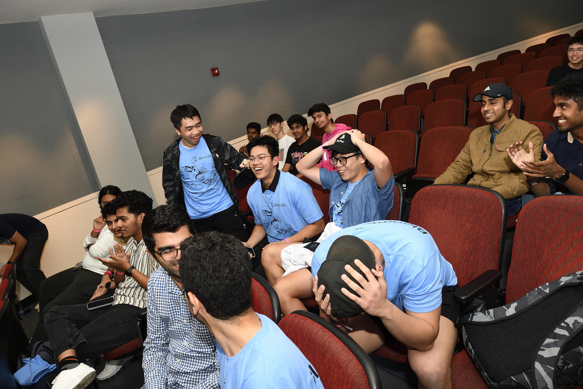 A team wearing matching light blue T-shirts reacts with happiness and shock in Hodson 110.