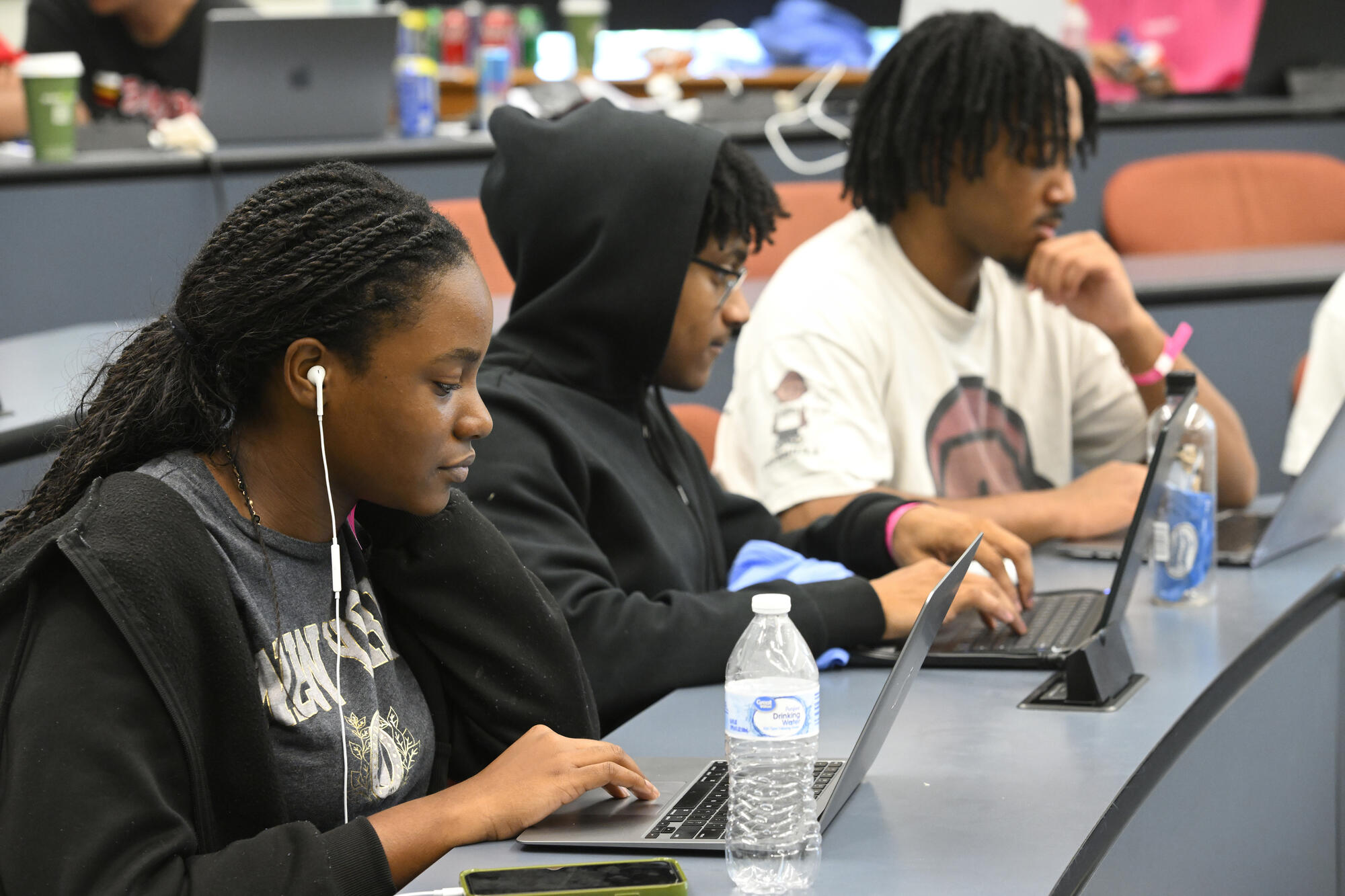 Three students stare intently at their laptops during HopHacks.