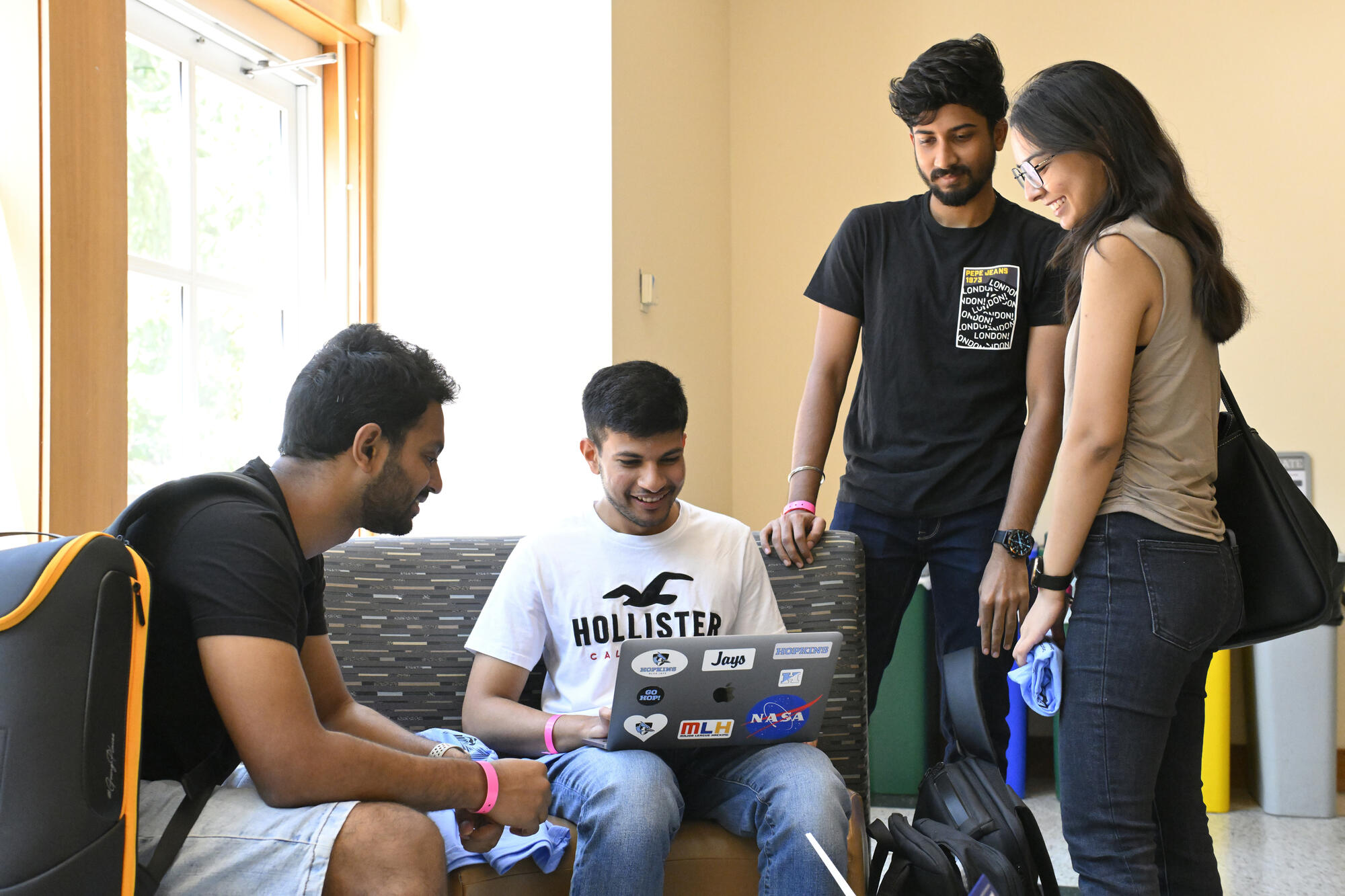 Students, two standing, two sitting, gather around a laptop in the Hodson Hall lobby.