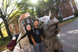 Students take a selfie with an inflatable triceratops on campus.