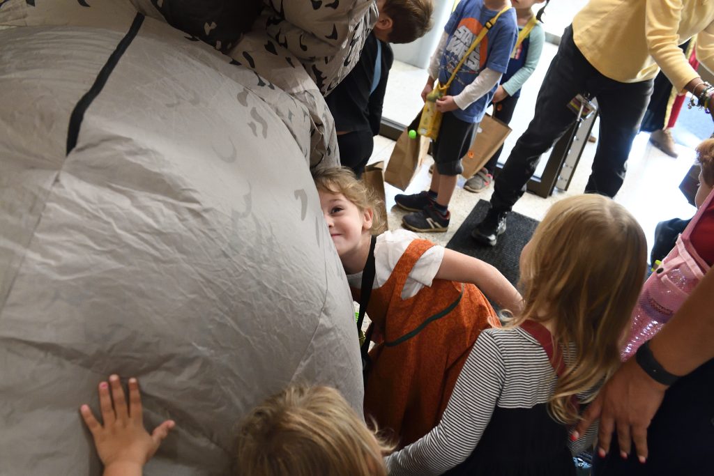 Trick-or-treaters pet and hug an inflatable triceratops.