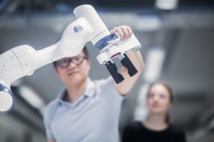 A student grasps a robotic arm's end effector as another student looks on.