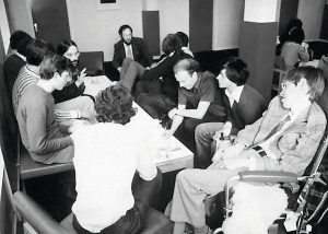 Black-and-white image of a room full of students supervised by Stephen Hawking.