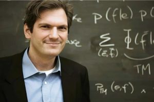 Philipp Koehn in front of a blackboard with equations written on it.